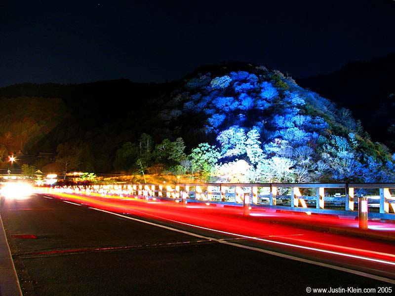 A car zooms over the bridge in Arashiyama lit up for a wintertime festival.