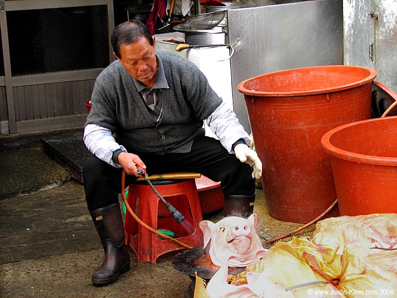A man blow-torching some pig heads.  Uh, wait a minute... 