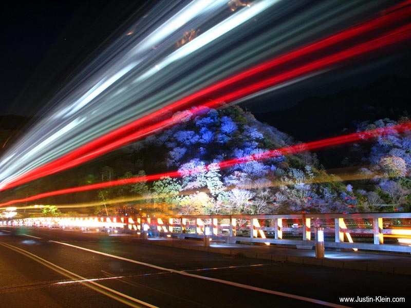 A city bus zooms by in front of an illuminated Arashiyama.