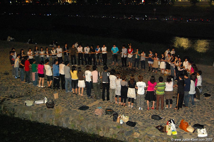 A group of students hold hands and cheer for the next volunteer to enter the circle and chug for everyone's amusement. 