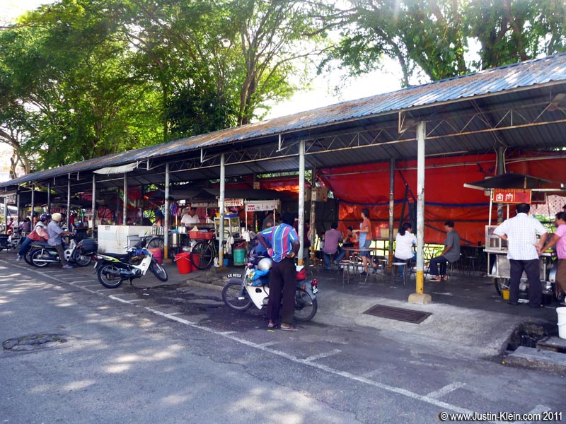 This is a *very* small example of a hawkwer court in a quiet suburb of Georgetown: Independent little carts or booths sharing a group of tables, where you have to buy a drink to sit down.